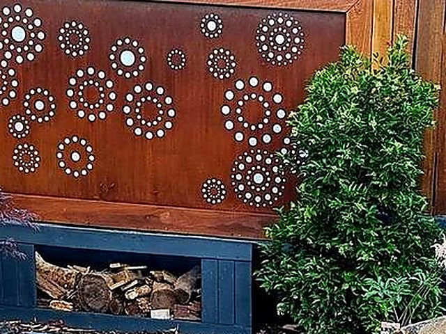 Corten steel screen with circular cut-outs above a timber log store