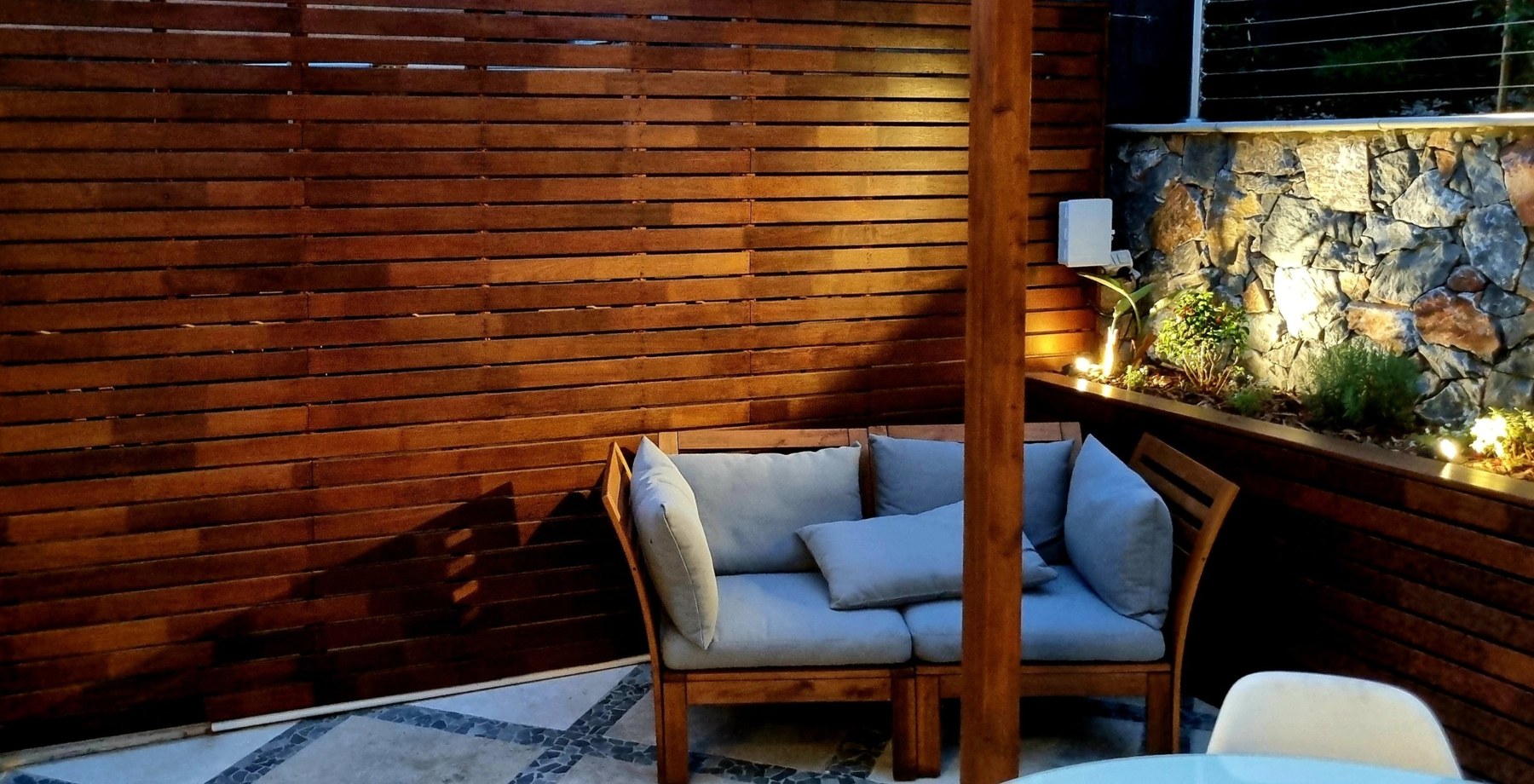Hardwood slat screen and timber planter box lit at dusk, with a timber post and outdoor seating